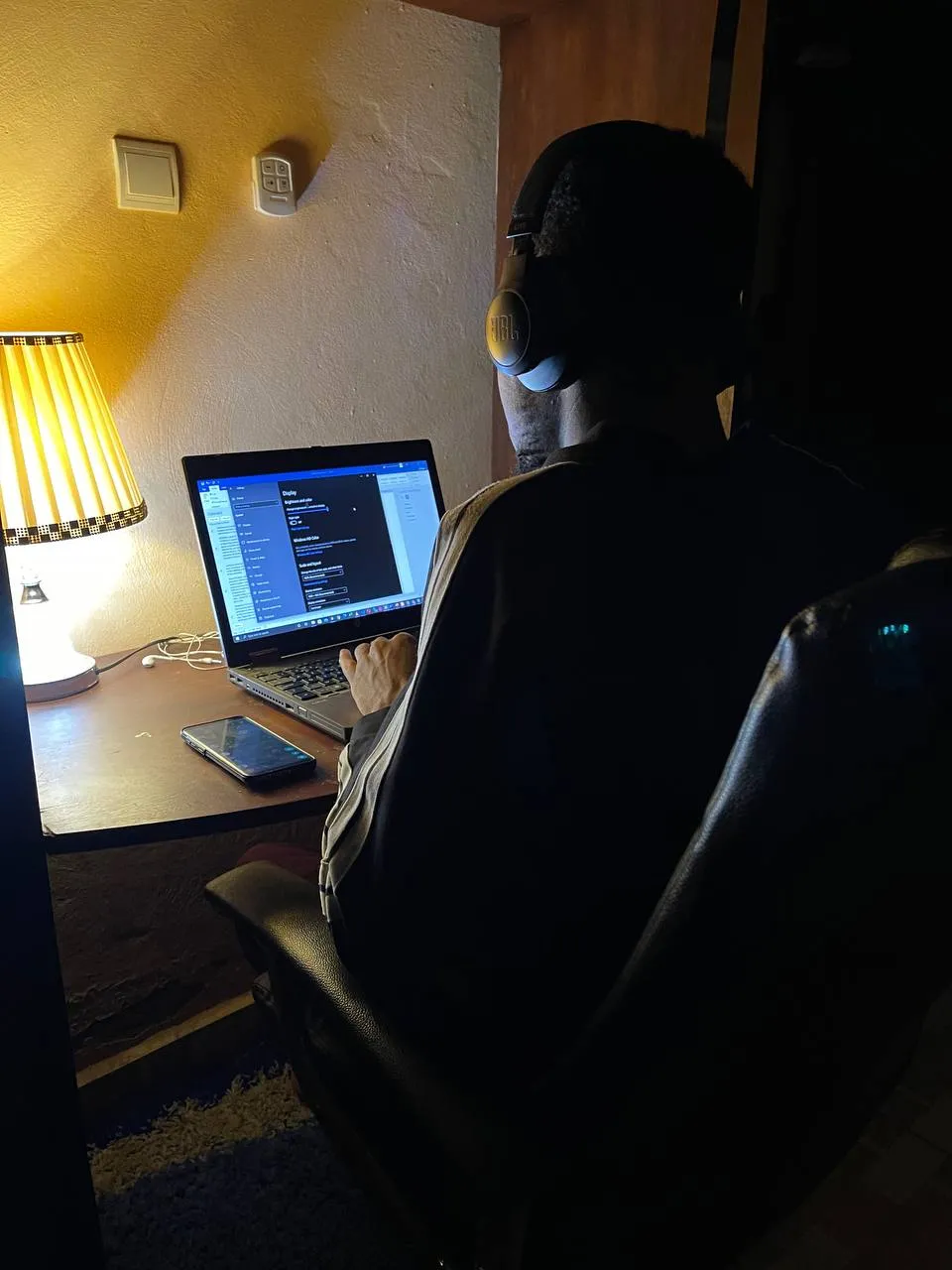 Nsom Emmanuel seen from behind, working on code at a laptop late at night
