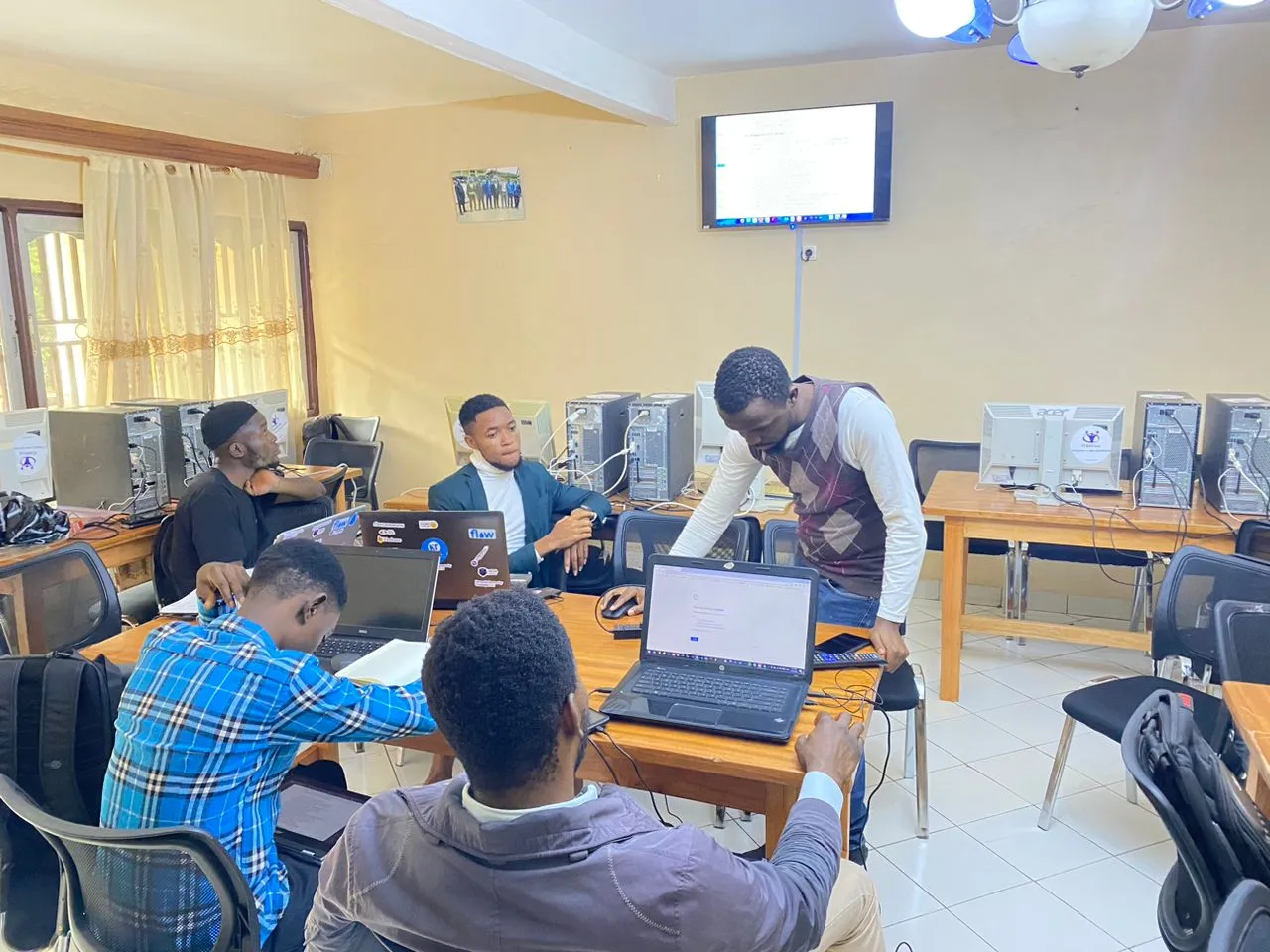 Trainees working at computers in a training room while Nsom Emmanuel guides one of them