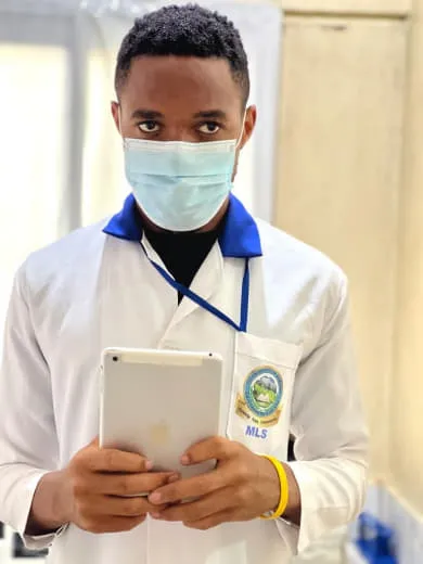 Nsom Emmanuel in a lab coat and face mask holding a tablet