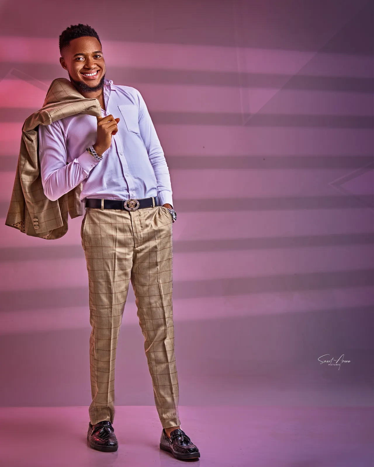 Nsom Emmanuel with a jacket over his shoulder against a pink studio backdrop
